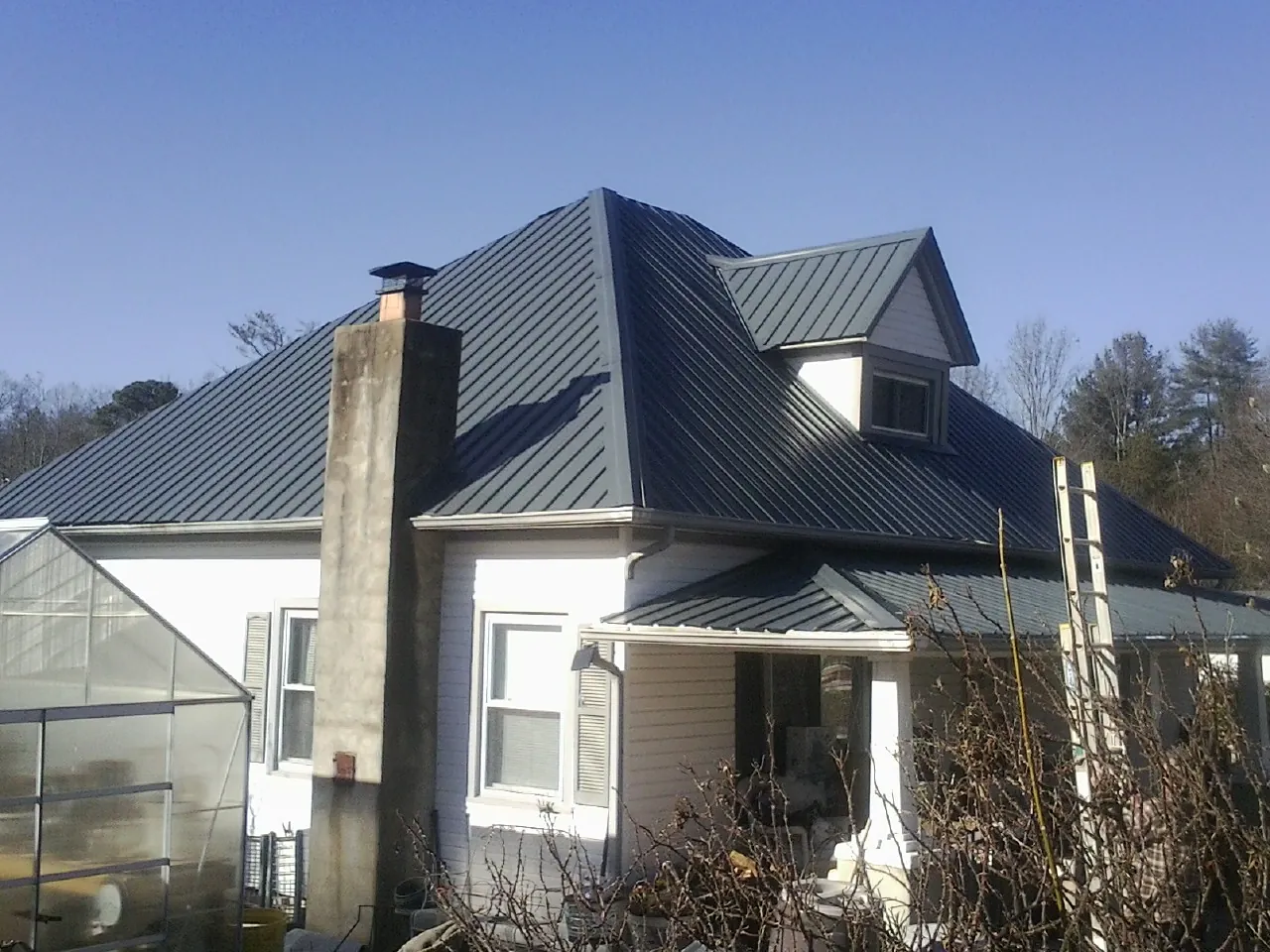 Dark blue standing seam metal roof on a white farmhouse with dormer — Slate & Tile Roof Repair by Roofing Brothers in Rialto