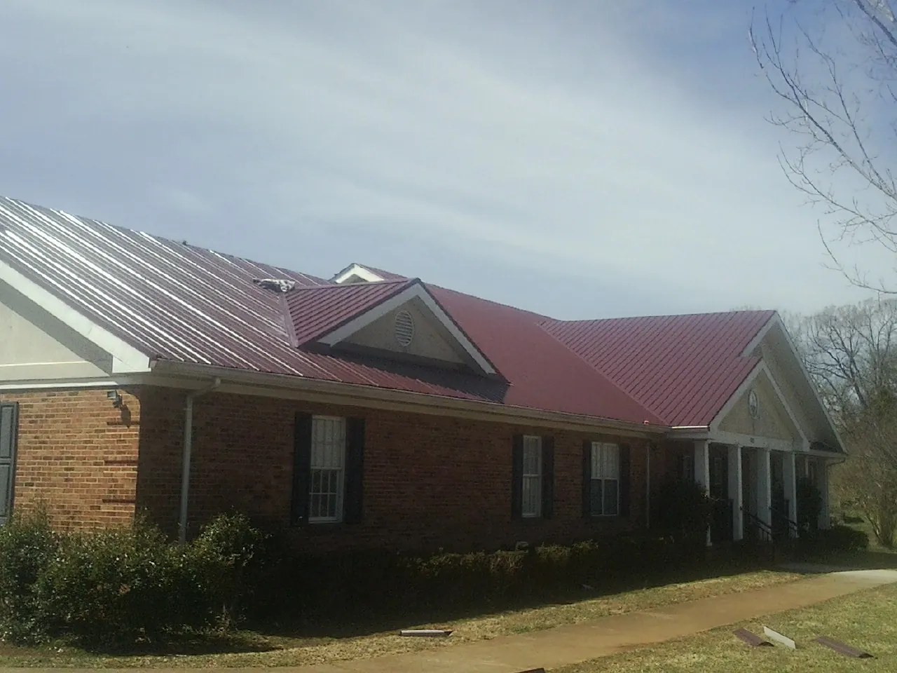 Red metal roof with gabled entries on a long brick building, from a Hail Damage Roof Repair job in Rialto
