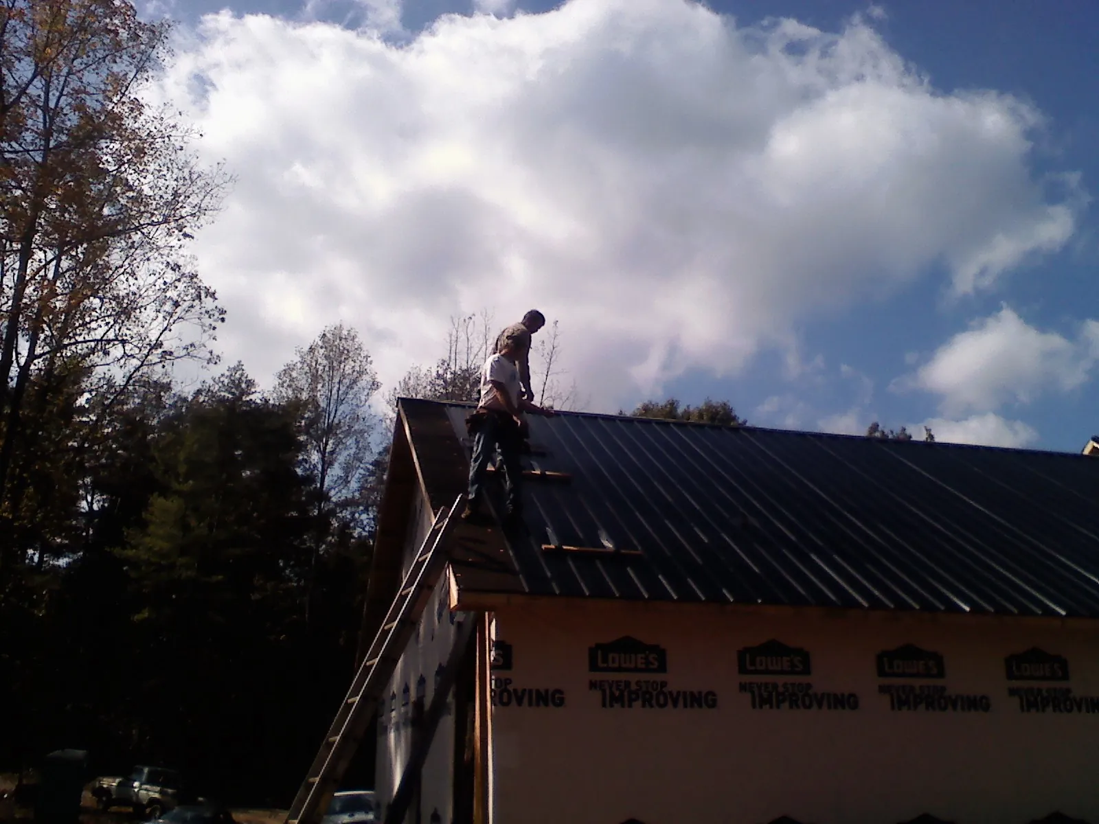 Roofer fastening dark metal panels high against a cloudy sky, from a Roof Inspection job in Rialto