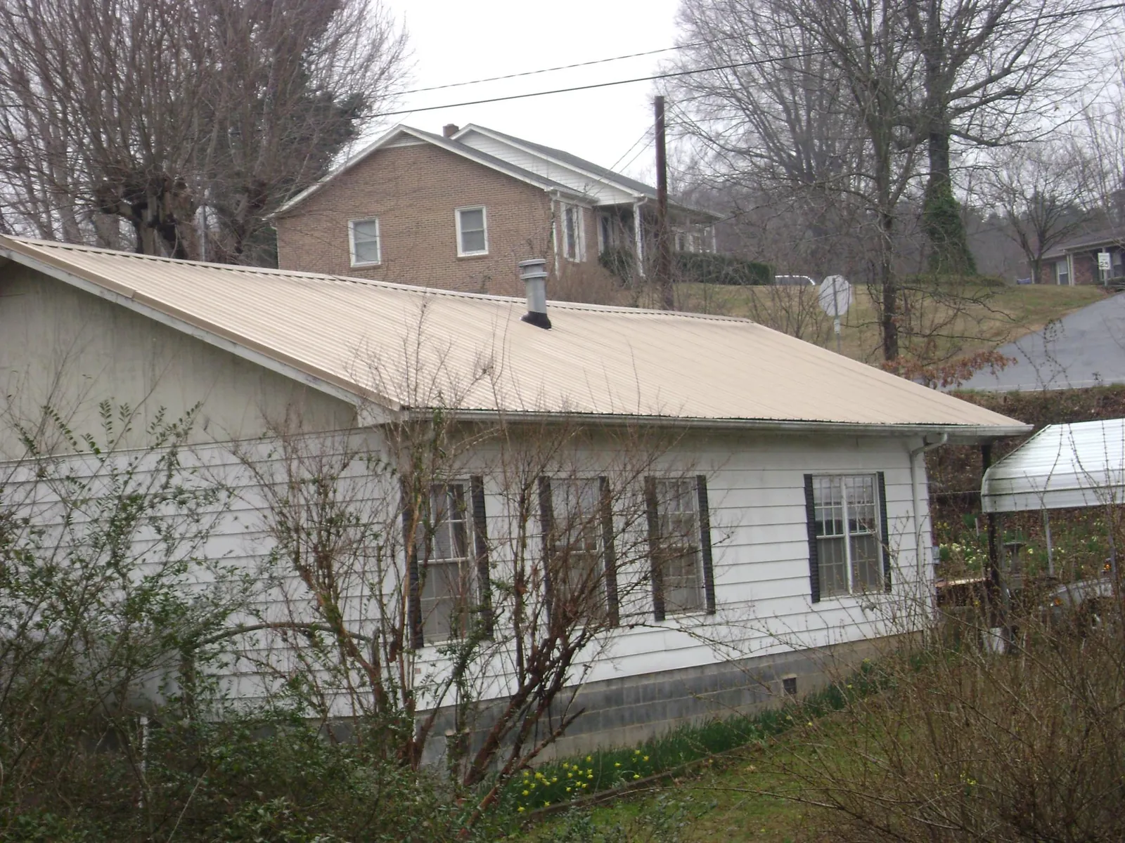 Tan metal roof on a white sided house set into a hillside — Commercial Roofing by Roofing Brothers in Rialto