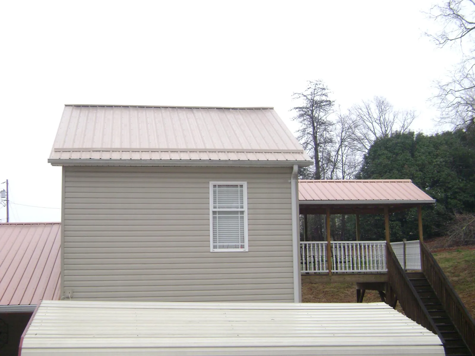 Tan metal roofs on a two story addition and attached porch, from a Roof Replacement job in Rialto
